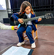 Aluna toca violão em aula de música
